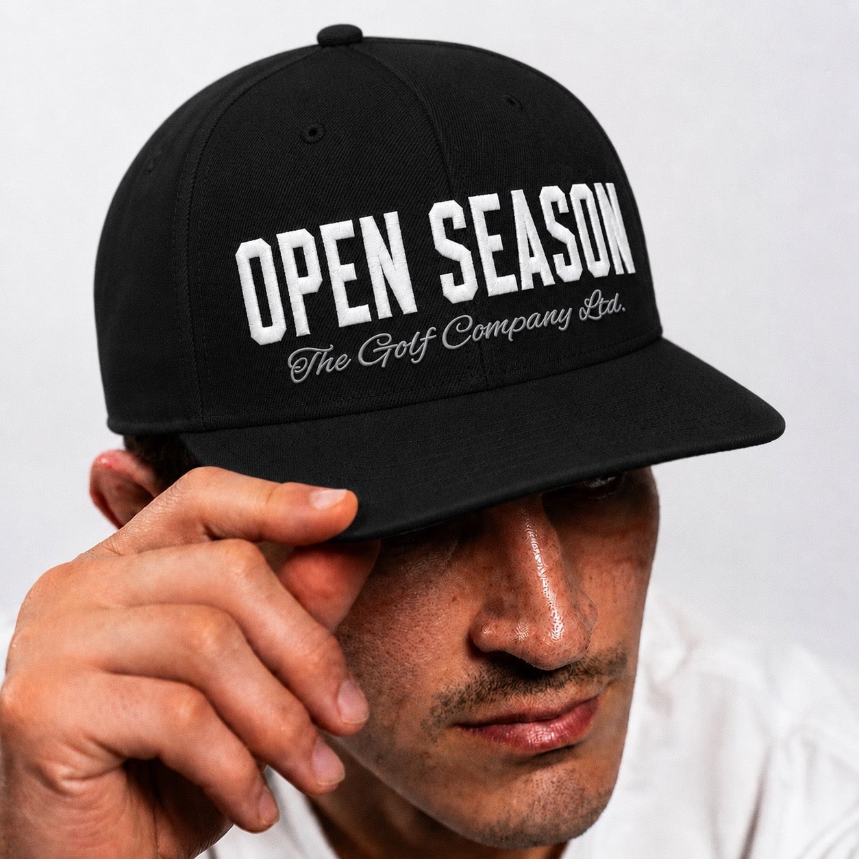 Black cap with 'Open Season' text held by a person against a white background