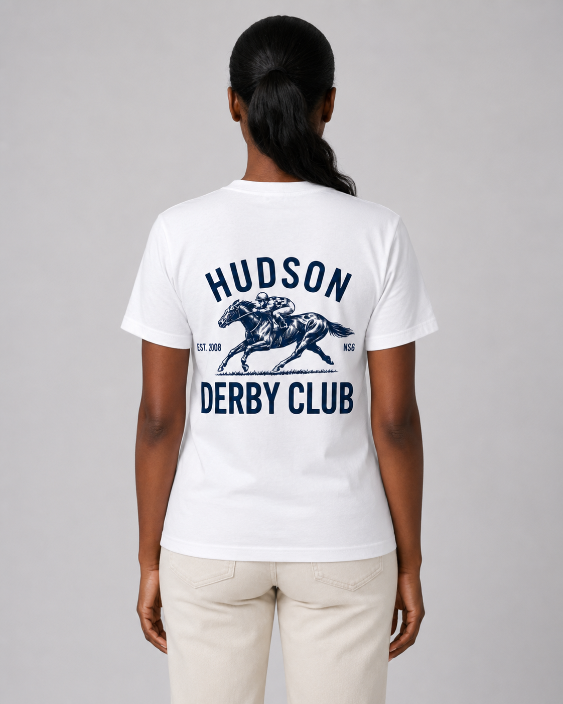 Person wearing a white t-shirt with 'Hudson Derby Club' text and graphic on the back, standing against a gray background.