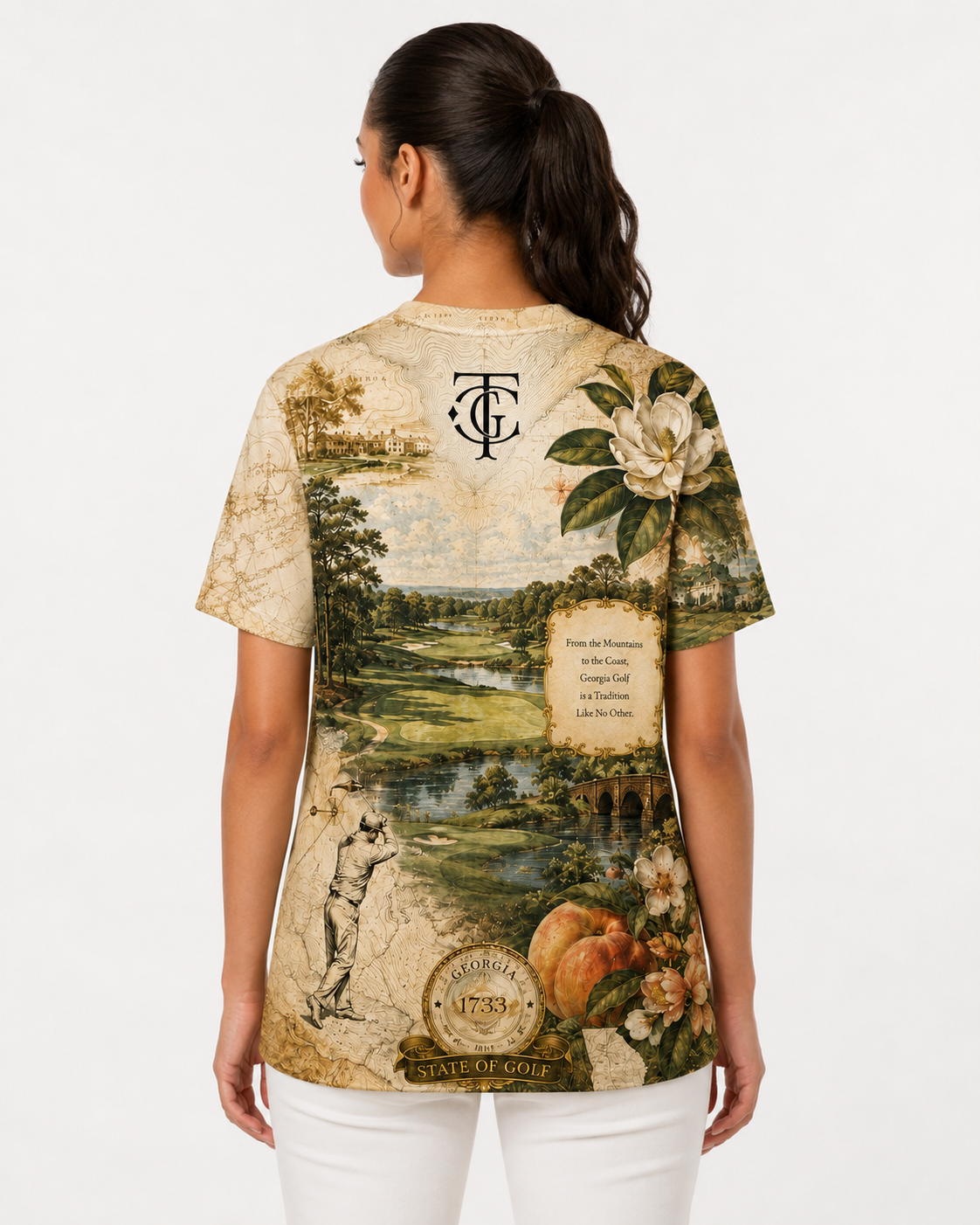 A woman viewed from the back wearing a vintage-style graphic t-shirt with a landscape print, white pants, and a ponytail, set against a plain white studio background.