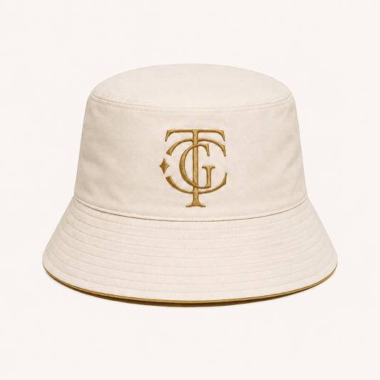 An off-white bucket hat featuring an embroidered gold monogram logo on the front, set against a solid off-white background.