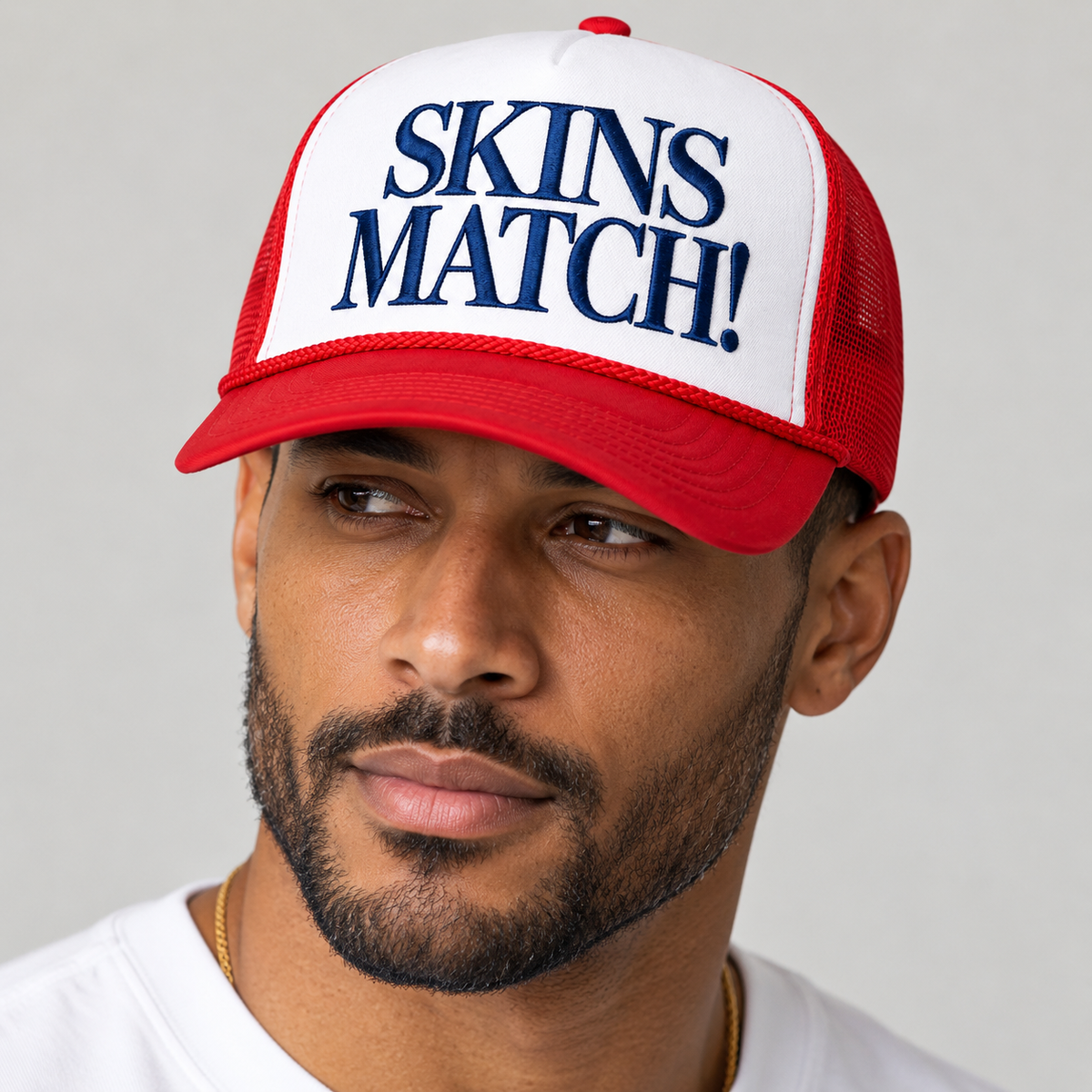 Biracial male wearing red and white SKINS MATCH trucker hat with navy embroidered lettering.