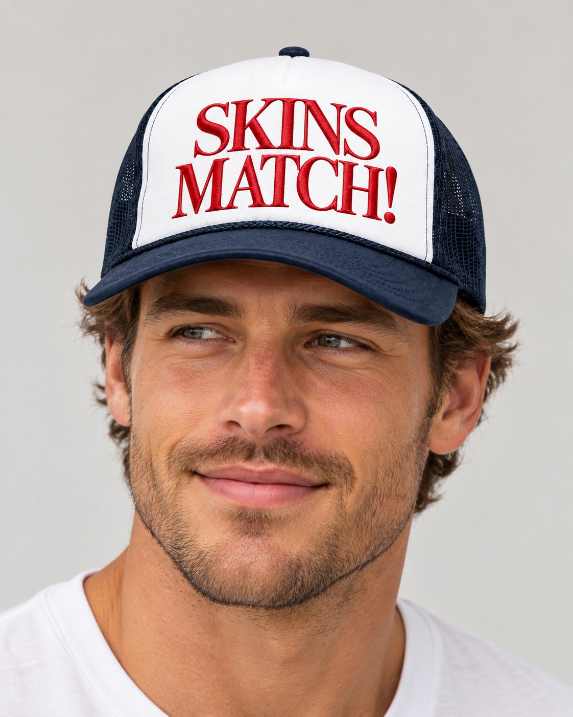 Caucasian male model wearing the Skins Match! navy and white trucker hat with red embroidery.