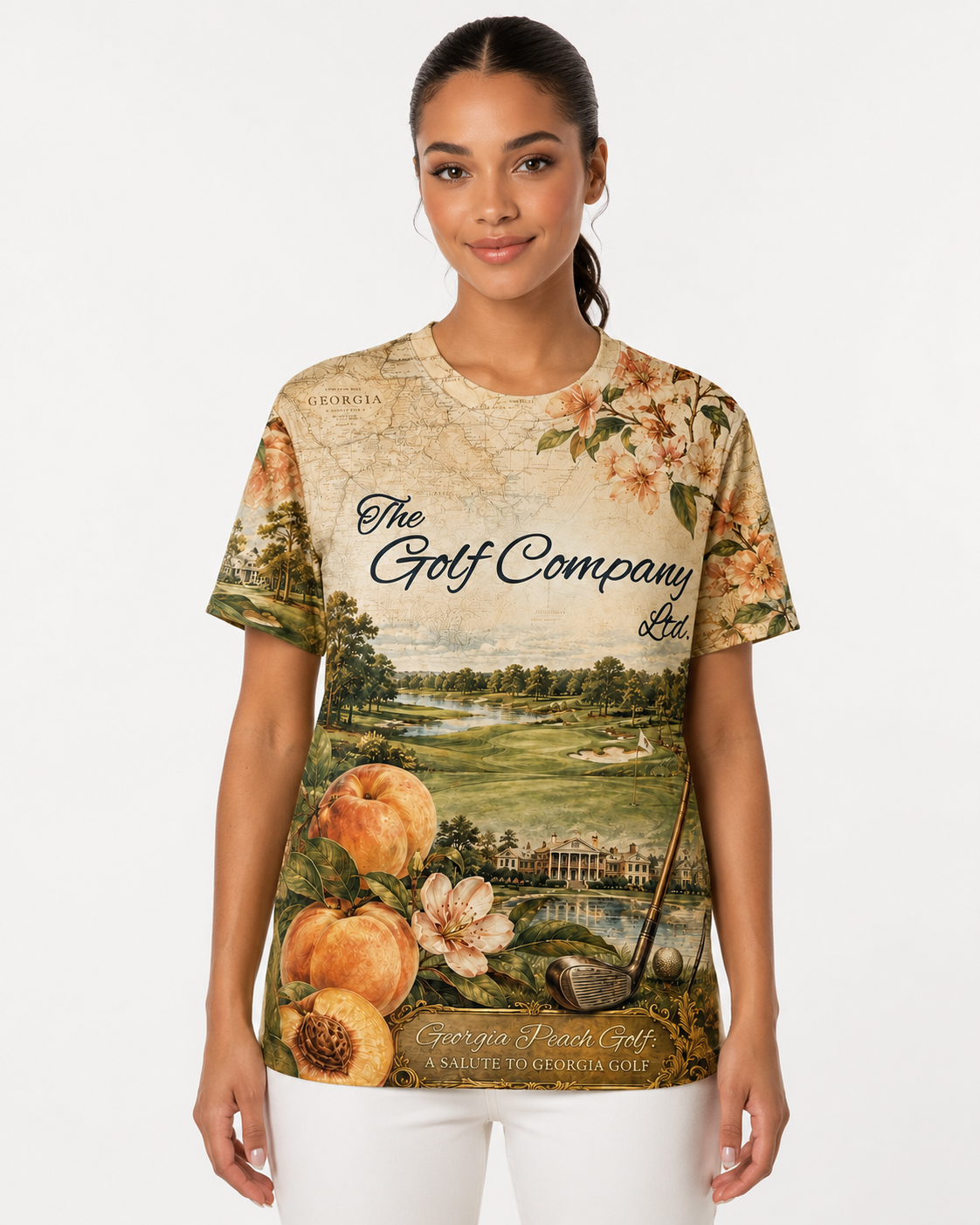 A woman modeling a short-sleeve graphic t-shirt featuring a vintage-style print of 'The Golf Company Ltd.' with a golf course landscape, peaches, and flowers on a cream background.