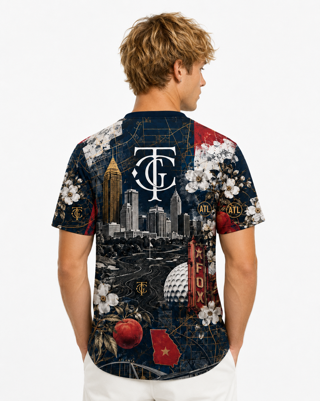 A man viewed from the back wearing a short-sleeve crewneck t-shirt with a complex, colorful collage print featuring the Tampa Bay Buccaneers logo, city skyline, and sports elements, paired with white pants against a light gray background.