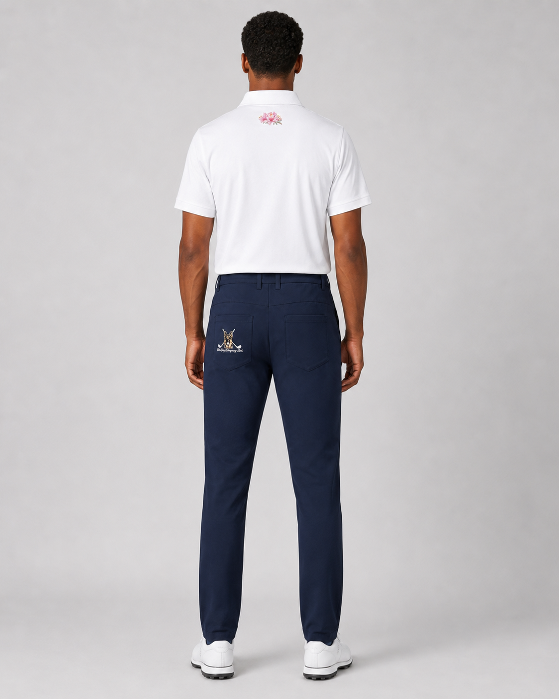 Man wearing a white polo shirt and navy pants with brand logos on a gray background