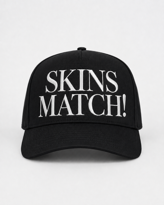 Black 5-panel snapback cap with white raised “SKINS MATCH!” embroidery on the front crown