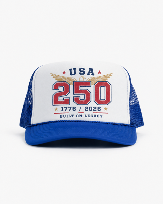 Royal blue and white USA 250 trucker cap with patriotic eagle artwork, red 250 lettering, 1776–2026 detail, and Built On Legacy text.