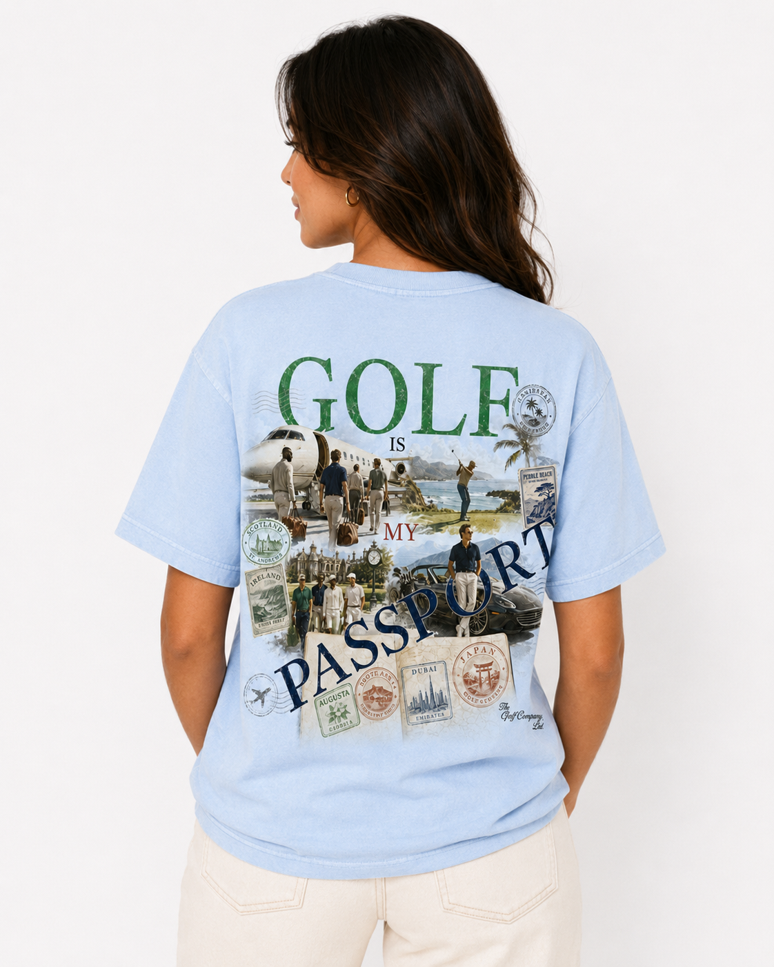 A woman shown from the back wearing a light blue graphic t-shirt with a large 'GOLF IS MY PASSPORT' design, paired with cream-colored pants, against a plain white background.
